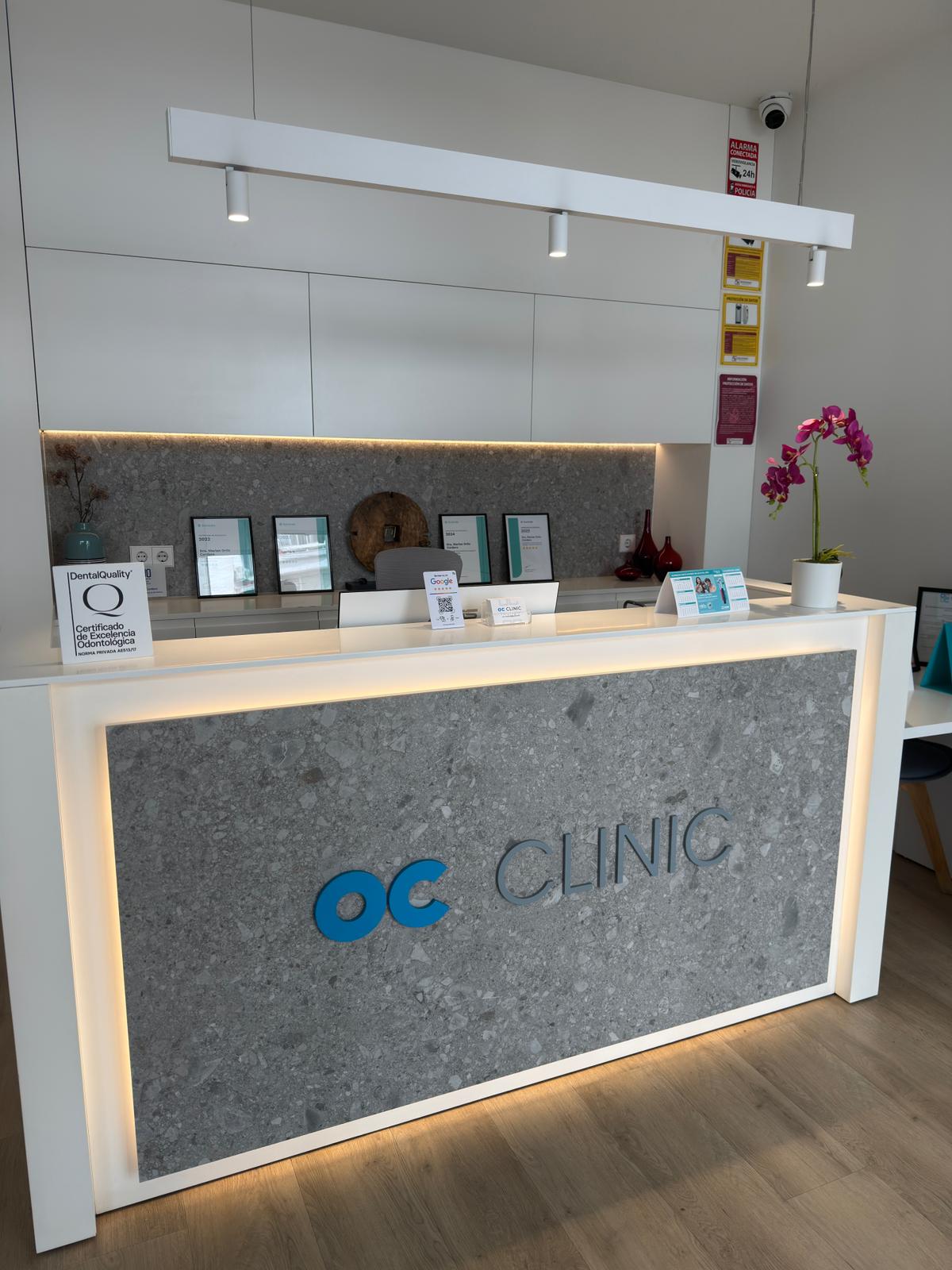Recepción de OC Clinic: mostrador acogedor, iluminación cálida y certificaciones a la vista